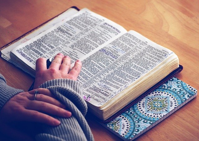 ręce kobiety leżące na stronach otwartej księgi, która może być Biblią